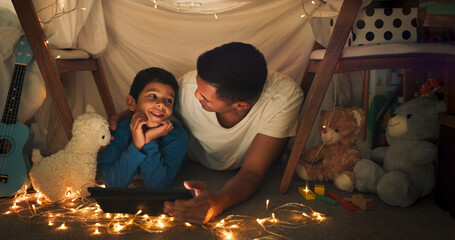 Dad and son at night on tablet in tent watching movies, online games and cartoon with fairy lights....