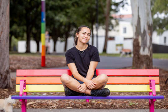 Aboriginal woman sitting cross-legged on a rainbow park bench
