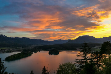 Fototapeta premium Panoramic sunset view on Lake Faak from Taborhoehe in Carinthia, Austria, Europe. Surrounded by high Austrian Alps mountains. Water surface reflecting soft sunlight. Remote alpine landscape in summer