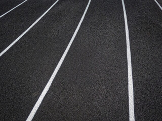 Fototapeta premium Track and Field Running Lanes. Overhead view of a rubber black running surface with white lane lines. There is a slight curve of the white lane lines. 