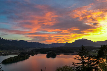 Panoramic sunset view on Lake Faak from Taborhoehe in Carinthia, Austria, Europe. Surrounded by high Austrian Alps mountains. Water surface reflecting soft sunlight. Remote alpine landscape in summer