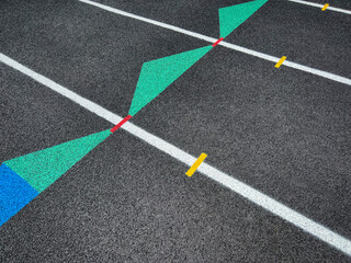 Angled overhead view of a rubber black running track surface with white lane lines. Green and blue arrows point forward. Red dashed line between the arrow shapes. Texturized rubber black surface.