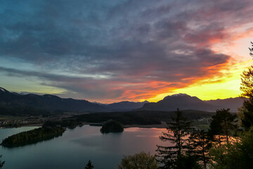 Panoramic sunset view on Lake Faak from Taborhoehe in Carinthia, Austria, Europe. Surrounded by high Austrian Alps mountains. Water surface reflecting soft sunlight. Remote alpine landscape in summer