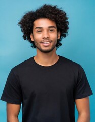 Fototapeta na wymiar Handsome brunette young man in simple black t-shirt with curly hair smiling to the camera isolated on blue background with copy space, good looking model portrait