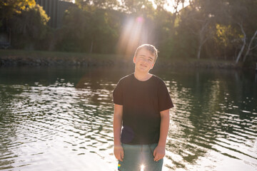 Teen boy standing in golden afternoon light by the water on holiday