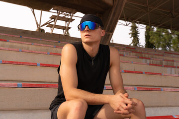 Runner sitting on the bleachers of a sports centre wearing sports clothes and blue running glasses. Sport concept of real people