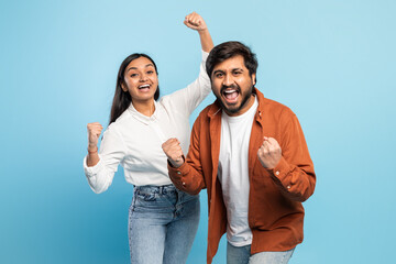 Couple cheering joyfully with raised fists on blue