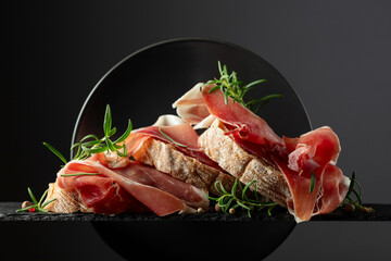Ciabatta with prosciutto and rosemary on a black background.