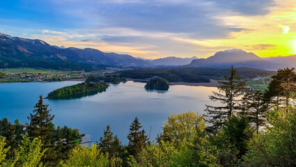 Panoramic sunset view on Lake Faak from Taborhoehe in Carinthia, Austria, Europe. Surrounded by high Austrian Alps mountains. Water surface reflecting soft sunlight. Remote alpine landscape in summer