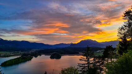 Panoramic sunset view on Lake Faak from Taborhoehe in Carinthia, Austria, Europe. Surrounded by high Austrian Alps mountains. Water surface reflecting soft sunlight. Remote alpine landscape in summer