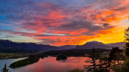 Panoramic sunset view on Lake Faak from Taborhoehe in Carinthia, Austria, Europe. Surrounded by high Austrian Alps mountains. Water surface reflecting soft sunlight. Remote alpine landscape in summer
