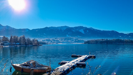 Snow covered wooden pier on lake Faak in Carinthia, Austria, Europe. Surrounded by high snow capped...