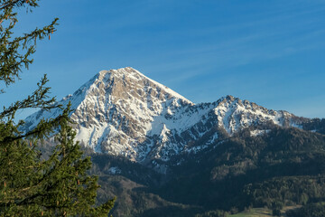 Fototapeta premium Panoramic view on snow capped mountain peak Mittagskogel Kepa seen from lake Faak in Carinthia, Austria, Europe. Alpine landscape in early winter. Snowfall in the Austrian Alps. Clear blue sky