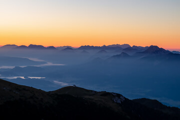 Panoramic sunrise view from Dobratsch on the Julian Alps and Karawanks in Austria, Europe. Silhouette of endless mountain ranges with orange and pink colors of sky. Jagged sharp peaks and valleys