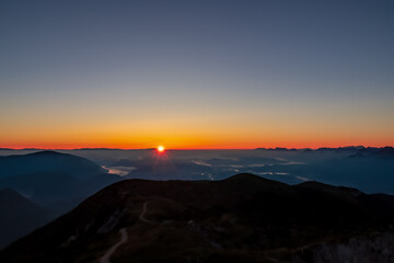 Panoramic sunrise view from Dobratsch on the Julian Alps and Karawanks in Austria, Europe. Silhouette of endless mountain ranges with orange and pink colors of sky. Jagged sharp peaks and valleys