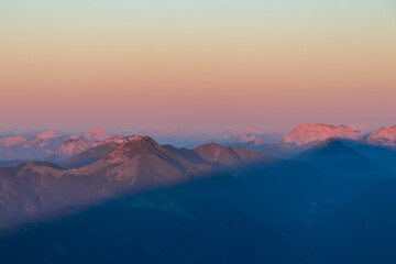Panoramic sunrise view from summit Dobratsch on Julian Alps and Karawanks in Austria, Europe. Silhouette of endless mountain ranges with orange and pink colors of sky. Jagged sharp peaks and valleys