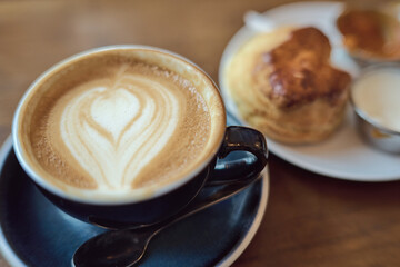 cup of cappuccino in a black cup with scones on a wooden table