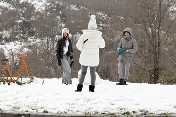 Three people are captured in a casual and candid manner as they enjoy a snowy day outside, each...