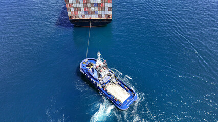 Aerial drone top down photo of tow - tug boat assisting by pulling container ship to dock to terminal port