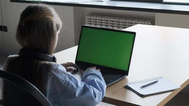 A young girl works at a laptop. Chromakey screen. Back view.