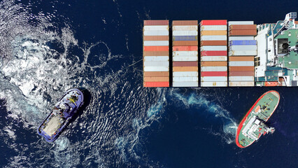 Aerial drone top down photo of tow - tug boat assisting by pulling container ship to dock to...
