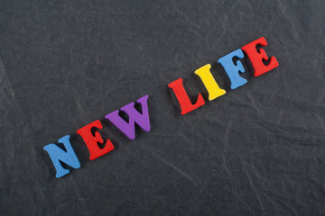 NEW LIFE word on black board background composed from colorful abc alphabet block wooden letters, copy space for ad text. Learning english concept.