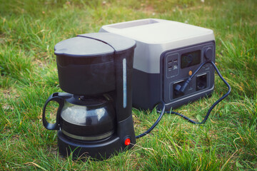 Making drip coffee in camp. The power station with electrical coffee maker on the grass. - 779981877