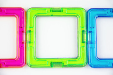 A group of 3 colorful transparent magnet squares (constructor for kids), green, blue and pink in a row, closeup on a white background