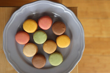Purple plate filled with pastel macarons on wooden table. Top view.