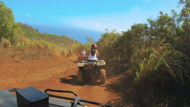 Driving an all-terrain vehicle on dusty orange road in the mountains and towards the ocean bay. Pov footage of ATV trip in West Maui Mountains, Hawaii.