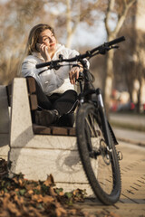 Woman Using Her Phone While Sitting on Bench Next to Bike