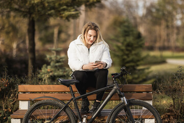 Woman Using Her Phone While Sitting on Bench Next to Bike