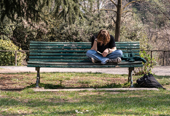 Student reading cross-legged on park bench.