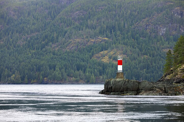 Red and white lighthouse stands in the water, guiding ships with its beacon