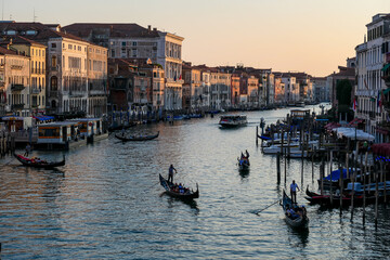Scenic sunset view of Grand Canal (Grand Canale) with tourist gondolas in Venice, Veneto, Italy, Europe. Famous landmark cathedral San Simeon Piccolo. Gondoliers at golden hour. Urban summer tourism - obrazy, fototapety, plakaty