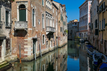 Floating boats with panoramic view of a water channel in city of Venice, Veneto, Italy, Europe. Venetian architectural landmarks and old houses facades along water canal. Urban tourism in summer - obrazy, fototapety, plakaty