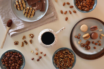 Cup of tea or coffee, cookies, macaroons, chocolate, various nuts and cocoa powder on white background. Top view.