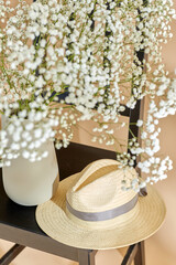 home decor and design concept - close up of gypsophila flowers in vase and straw hat on vintage...