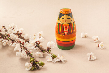 A souvenir stylized as a Tatar girl next to flowering branches of forsythia and cherry plum on a gray background. Mass production. Navruz holiday concept
