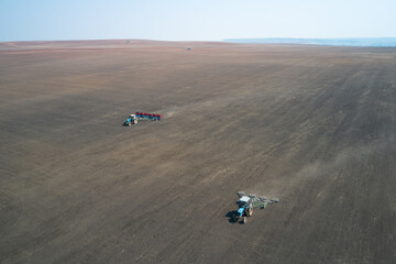 Sowing campaign. Sowing wheat in the field. Behind the tractor with a seeder works tractor with rollers. Shooting from a drone. - obrazy, fototapety, plakaty