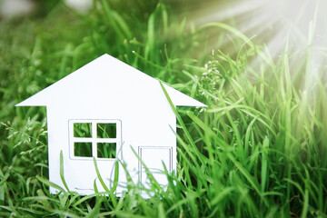 The concept or conceptual house white paper in his hand in a green summer grass on a background, a symbol for the construction, environment, credit, property or home