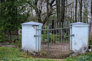 old crooked cemetery gate with white columns. Jačūnu kapi, Latvia, Zemgale
