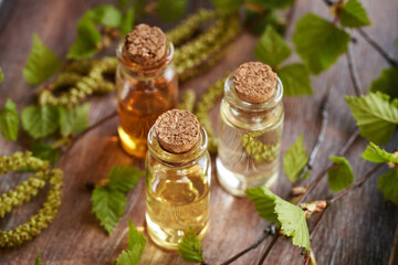 Three bottles of essential oil with birch tree branches with catkins and young leaves harvested in...