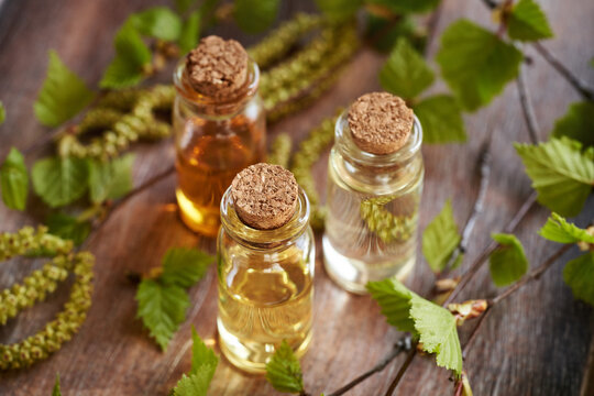 Three bottles of essential oil with birch tree branches with catkins and young leaves harvested in spring
