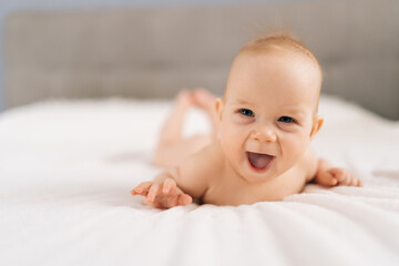 Cheerful infant baby lying on bedroom bed, enjoying morning relaxation indoor at home, looking at...