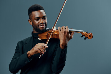 Elegant African American man in black suit playing violin on gray background, creating beautiful...
