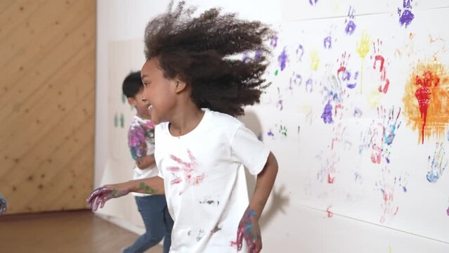 Playful children playing and running with colorful stained hand in front of white background. Funny happy multicultural students enjoy attending in art lesson. Creative activity concept. Erudition.