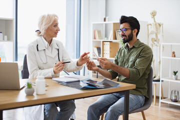 Senior female general practitioner communicating with young patient holding bottle and blister of...