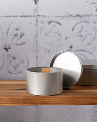 A candle in a tin box with a wooden wick on a wooden shelf in the bathroom