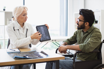 Attractive bearded young man looking on tablet with x-ray image carried by radiologist in...